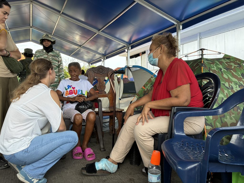 A woman crouching talking to two other women in a relief camp