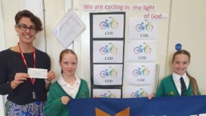 A woman holding a cheque next to schoolchildren and with posters behind