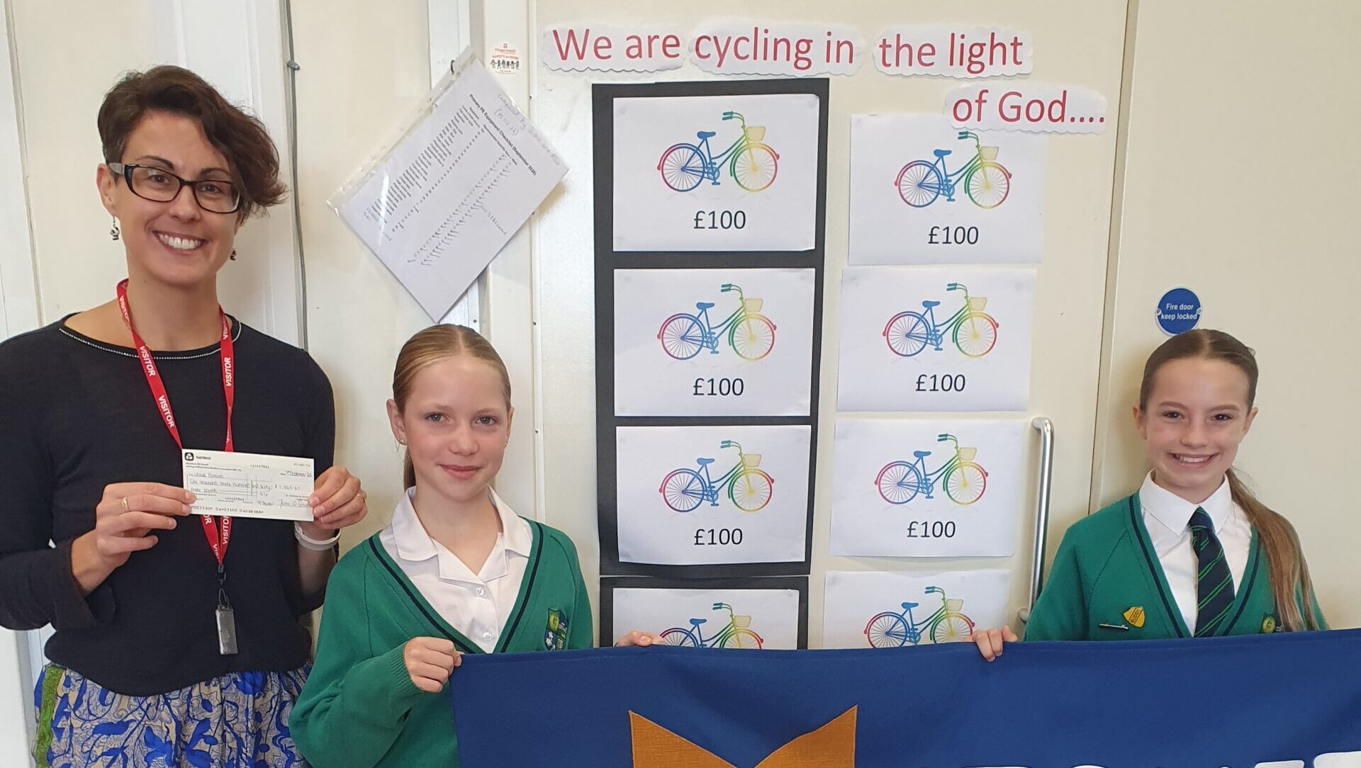 A woman holding a cheque next to schoolchildren and with posters behind