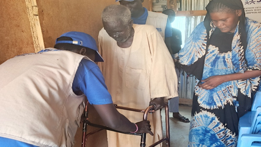 A man holding a walking frame being helped by two people.