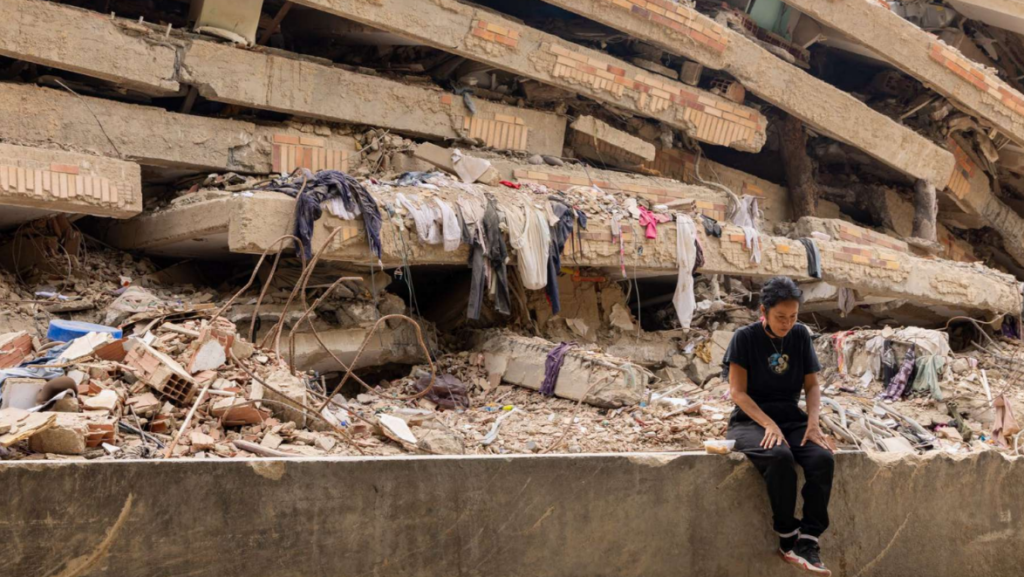 A person sitting on a wall next to a collapsed building